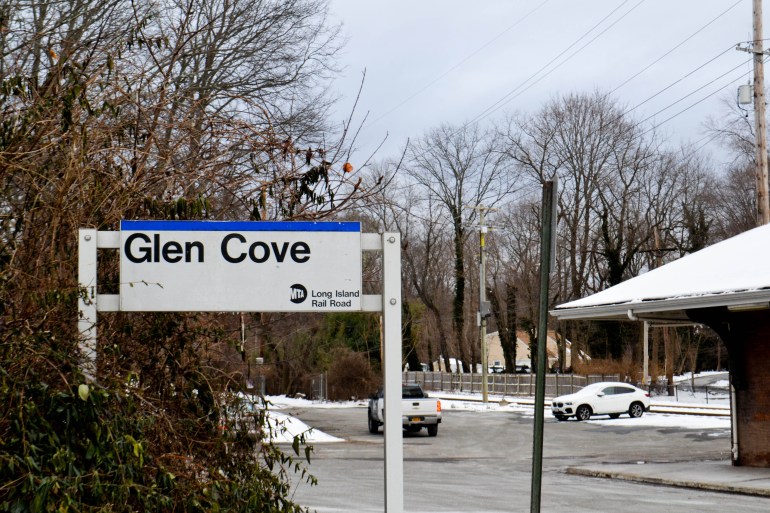 تقف لافتة مكتوب عليها "Glen Cove" بجانب موقف السيارات والطريق بعد تساقط الثلوج الطازجة.