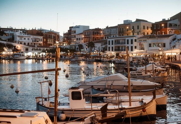 منظر القوارب المتمايل بالقرب من Es Castell Harbour عند الغسق ، مع المباني في الخلفية 