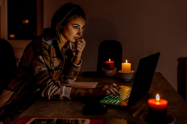 تعمل امرأة شابة خلال أزمة كهرباء تسبب تعتيمًا تحت الشموع المضاءة باستخدام جهاز كمبيوتر محمول.