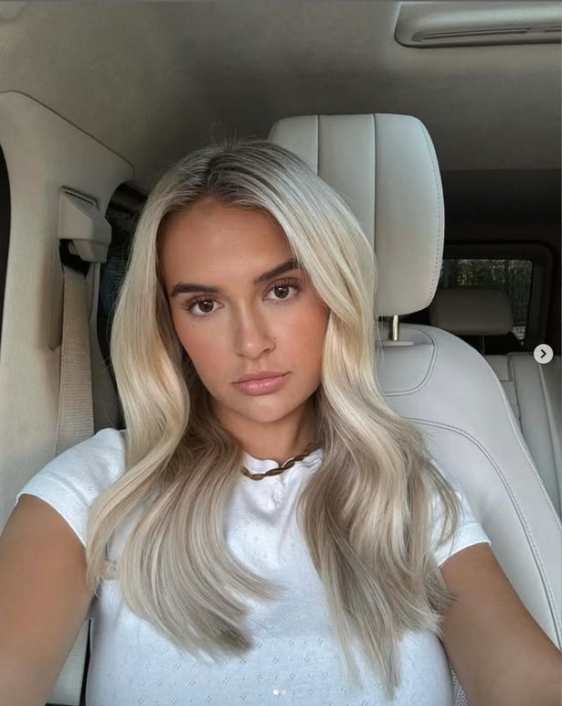 جلس مولي ماي لاهاي في قميص أبيض في سيارة في صورة شخصية.
