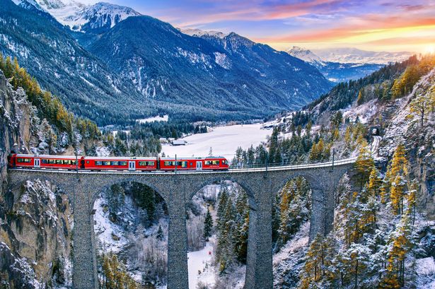 المنظر الجوي للقطار الذي يمر عبر الجبل الشهير في فيليزور ، سويسرا. Landwasser Viaduct World Heritage With Train Express in Swiss Alps Snow Winter Clainery.
