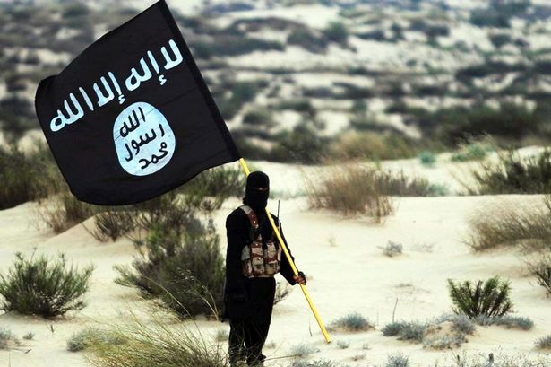 يطرح جندي من دولة إسلامية مقنعة لافتة داعش في مكان ما في صحراء العراق أو سوريا.