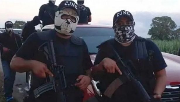 رجلان يرتديان القمصان السوداء وأغطية الوجه وقبعات سوداء مع CJNG في النص الأبيض يقف أمام سيارة حمراء تحمل بنادق