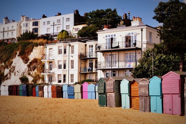 الخزائن الشاطئية الملونة في Broadstairs في يوم مشمس في سبتمبر 2013 ، والرمال في المقدمة مع صف الخزائن الشاطئية/الأكواخ في الخلفية التي تبرزها السماء الزرقاء الصافية.