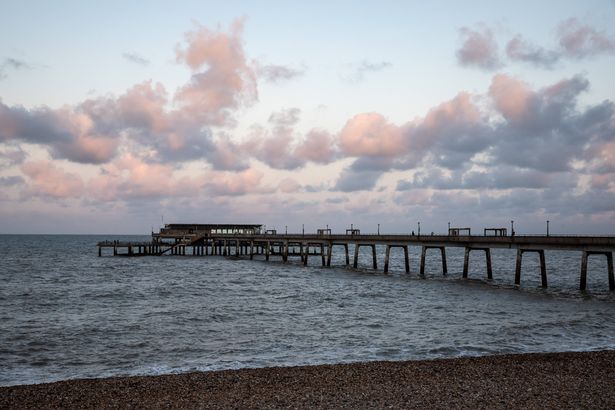 يمتد Pier Deal Pier في إنجلترا إلى البحر ، ويقدم مشهدًا خلابًا. السماء ، المزينة بالغيوم ، تخلق أجواء غائمة. تأخذ السماء الزرقاء الفاتحة اللون الوردي الدقيق أثناء وضع المساء. تظهر المياه الهادئة بلون بلون رمادي ، تموج بلطف مع موجات صغيرة. يوفر الرصيف ، الذي يمتد إلى المسافة ، نقطة محورية في التكوين. محاط بالماء ، يقف كرمز للسحر الساحلي. . الأفق مرئي في المسافة ، ويوفر شعورًا بالعمق والمساحة. يغطي القوباء المنطقية الشاطئ ، واستكمال المناظر الطبيعية الساحلية.