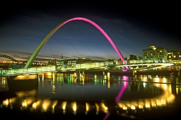 منظر من Gateshead باتجاه نيوكاسل من جسر الألفية المضيئة في الليل المنعكس في نهر تاين.