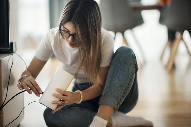 منظر المقربة للسيدات في منتصف الثلاثينيات تحاول إصلاح جهاز جهاز التوجيه الشبكي في المنزل.