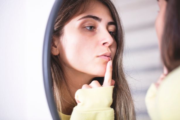 المرأة التي تطبق كريمًا باردًا على الشفاه أمام المرآة