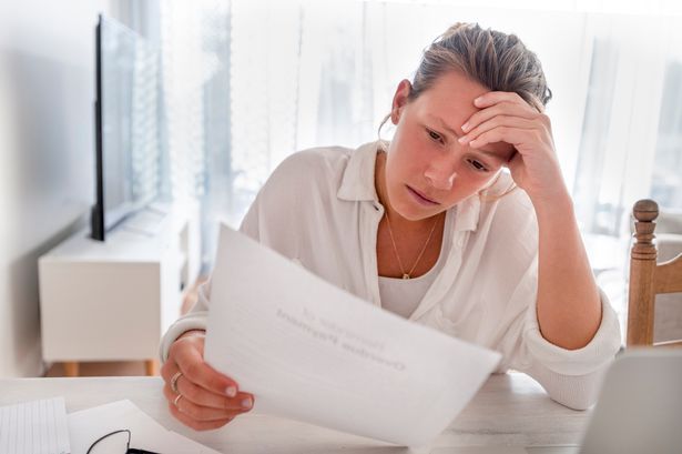 امرأة تبدو قلقة في عقد الأوراق في المنزل. إنها تقرأ فاتورة مالية أو خطاب مع أخبار سيئة. انها تبدو متوترة جدا ومزعجة. يوجد كمبيوتر محمول على الطاولة
