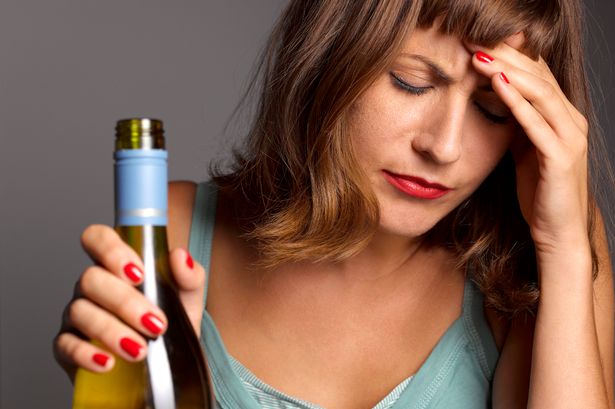 امرأة تحمل زجاجة من النبيذ وتمسك رأسها