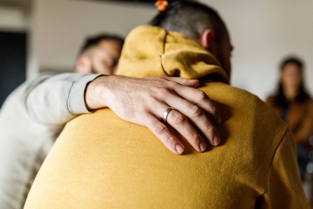 عن قرب لقطة من الرجل الرحيمة الذي يحتضن صديقه الذي يشارك قصة ثقيلة فيما يتعلق بصحته العقلية خلال جلسة علاج جماعية.