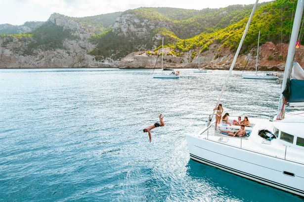 Aerial View with Drone of a Friends Friendsing مع سفينة طواف في جزيرة Ibiza ، خلال الإجازات الصيفية التي تستمتع بها والاستمتاع بالسباحة في الماء.