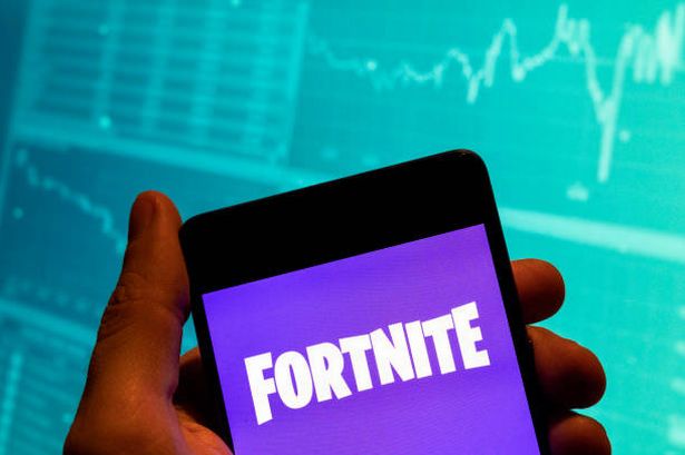 يتم عرض لعبة الفيديو عبر الإنترنت من قبل شركة Epic Games Fortnite Logo معروضة على هاتف ذكي مع رسم بياني مؤشر Exchange Exchange في الخلفية.