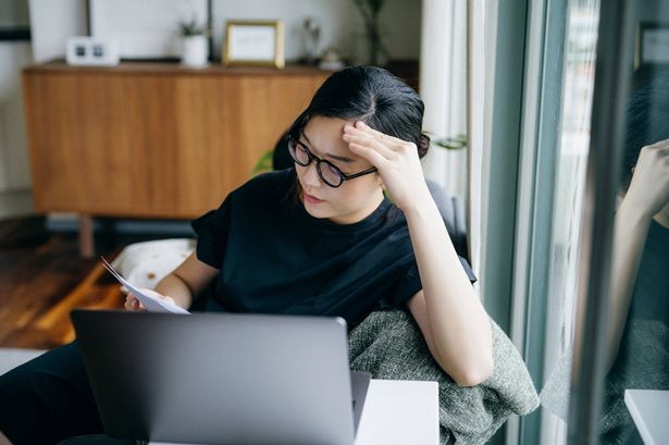 امرأة شابة تبدو متوترة أثناء إدارة فواتيرها المالية والوثائق الضريبية ، التي تجلس أمام الكمبيوتر المحمول في المنزل