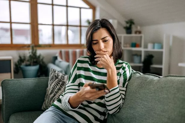 سيدة شابة من أصل إسباني شابة تبحث على شاشة الهواتف الذكية التي تتمتع بالدخرات المالية التي سرقت من البنك كنتيجة احتيال للمال
