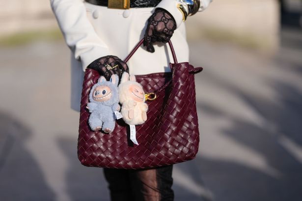 ضيف يرتدي حقيبة جلدية Borgundy Bordeaux Bottega Veneta Andiamo ، وسحر حقيبة Labubu الأزرق الفاتح ، وسحر حقيبة Labubu Cream ، خارج Elie Saab ، خلال أسبوع الموضة في باريس يوم 8 مارس ، 2025