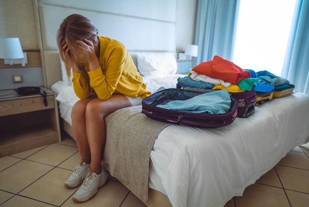 امرأة مستاءة جالسة على السرير مع حقائب مع ملابس.    