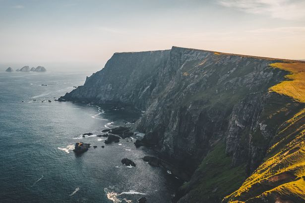 Benwee Head ، Co Mayo ، Ireland. تُرى المنحدرات الطويلة على اليمين مع محيط مظلم على اليسار وسماء زرقاء صافية أعلاه