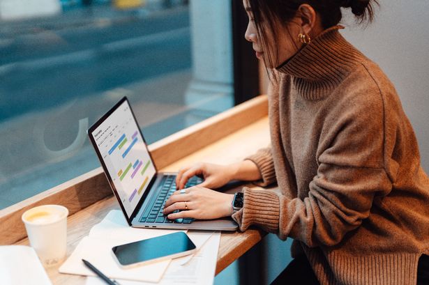 مديرة المتاجر الإناث تخطط لخطة العمل مع الكمبيوتر المحمول ، جالسة بجوار النافذة في المقهى.