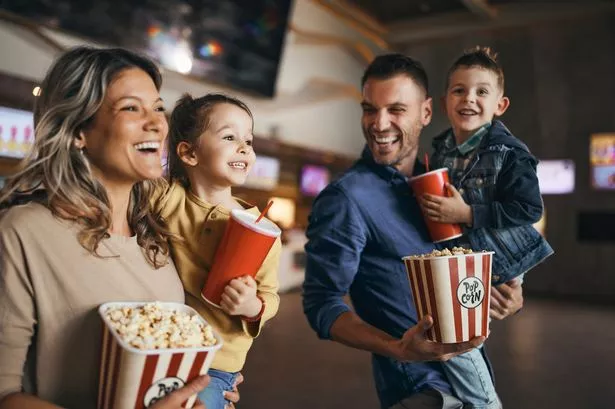 عائلة سعيدة تستمتع أثناء المشي مع الفشار والمشروبات في السينما.