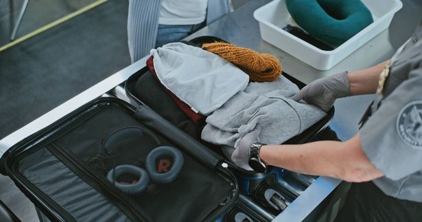 نقطة تفتيش أمنية في محطة المطار الدولية: مسؤول الأمن يفحص حقيبة الركاب على حزام النقل لمسح الأشعة السينية. إجراءات فحص الأمتعة TSA. زاوية عالية عن قرب.
