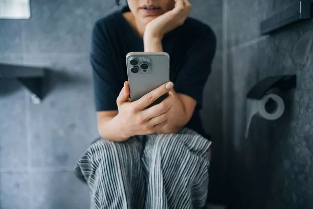 امرأة شابة تستخدم هاتفها الذكي أثناء الجلوس على المرحاض في الحمام