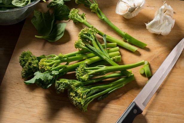 Tenderstem Broccoli ، والثوم ، وسكين حاد على لوح خشبي.