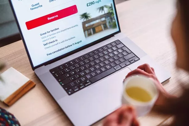 المرأة الآسيوية المبهجة حجز الإقامة على تطبيق السفر والتخطيط لقضاء عطلتها على الكمبيوتر المحمول في المنزل. 