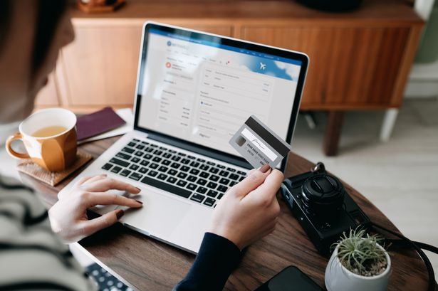 على المنظر الكتف للمرأة الآسيوية الشابة التي تتسوق عبر الإنترنت للحصول على تذاكر الطيران على موقع الطيران مع الكمبيوتر المحمول ، مما يدخل تفاصيل بطاقة الائتمان لجعل الدفع عبر الهاتف المحمول في المنزل. الكاميرا وجواز السفر على الطاولة. تخطيط السفر. حجز عطلة عبر الإنترنت