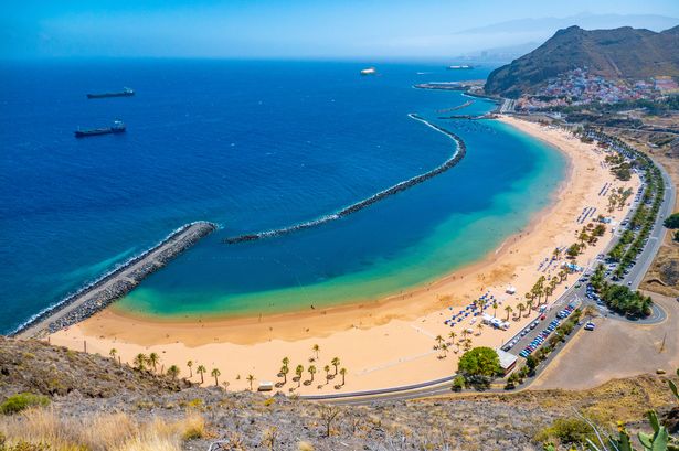 Las Teresitas Beach Panorama View من نقطة مشاهدة Mirador Playa de Las Teresitas ، بالقرب من سانتا كروز في جزيرة تينيريفي بركانو ، جزر كاناري في إسبانيا. Las Teresitas هو شاطئ بالقرب من قرية سان أندريس ، أحد أكثر الشواطئ شعبية في جزر الكناري للسكان المحليين والسياح مع الرمال البيضاء. إنه شاطئ اصطناعي مع رمال من صحراء الصحراء الغربية ، وهناك رصيفان ومياه طويلة لمنع موجات الشاطئ ، ويضم الشاطئ ثلاثة أجزاء ، و Los Moros ، و Tras La Arena ، و Ravine of Las Teresas. مياه بحر المحيط عريضة ، واضحة تمامًا مع أشجار النخيل ، وحانات الشاطئ ، والرياضات المائية والعديد من المرافق مما يجعلها مثالية للسياحة والعطلات. (تصوير نيكولاس إيكونو/نورفوتو عبر غيتي إيمايز)