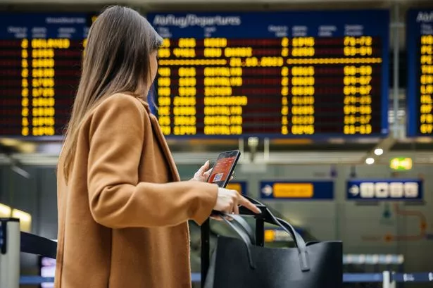 تقوم امرأة مسافر بفحص هاتفها المحمول أمام لوحة معلومات الطيران بالمطار ، وتستعد لرحلتها الفردية القادمة.