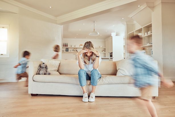 الأم التي تجلس على الأريكة بينما يركض أطفالها ADHD حول غرفة المعيشة