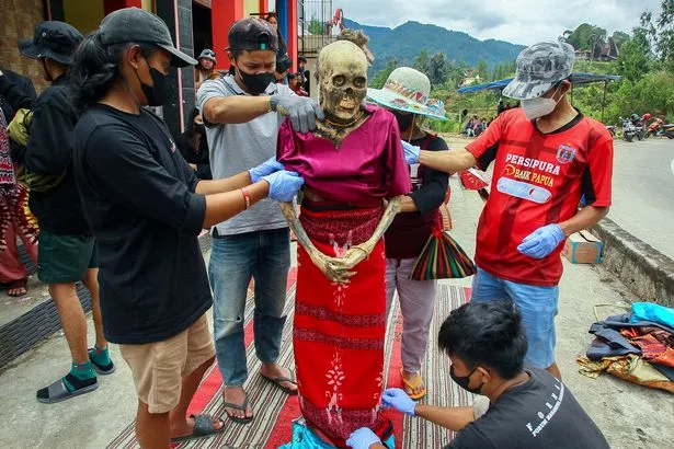 المحتوى الرسومي / أفراد الأسرة من مجموعة Toraja العرقية يتعاملون مع جسم قريبهم المتأخر ، تم استخراجهم من موقع الدفن ليتم تنظيفهم وارتداءهم في سلسلة من الاحتفالات التقليدية التي تكريم الموتى المعروفة باسم "ma'nene"، في قرية Lempo Po'ton في شمال توراجا ، جنوب سولاويزي ، 
