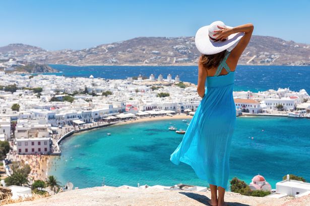 امرأة ترتدي ثوبًا أزرق تقف على جرف يطل على Mykonos