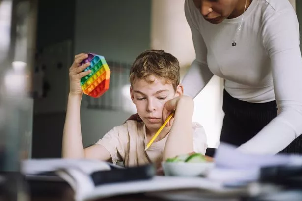 امرأة تساعد صبيًا صغيرًا يحمل لعبة البوب ​​أثناء قيامه بإجراء دراسته في المنزل