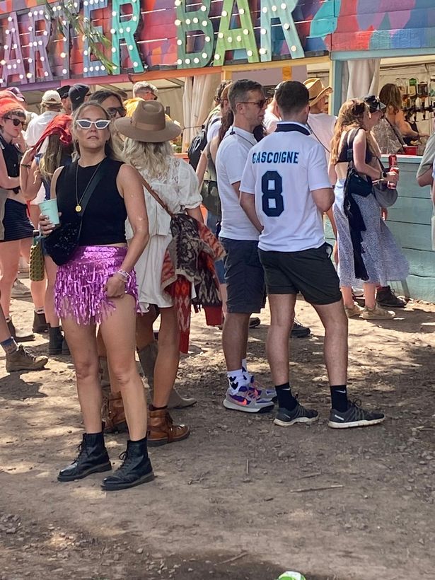 وقفت هولي ويلوغبي ، في ثوب أبيض ، في قائمة الانتظار للحصول على بار في Glastonbury 2025.