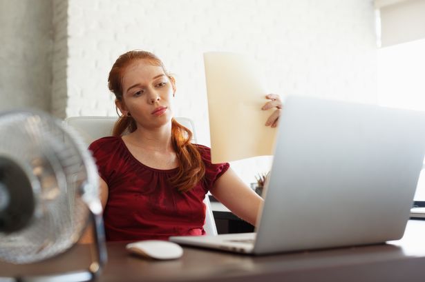 امرأة تعمل مع الكمبيوتر المحمول الكمبيوتر في المكتب في الصيف خلال موجة Heatwave. درجة الحرارة ساخنة وكسر مكيف الشعر. الفتاة تعرق وتشعر بالإرهاق