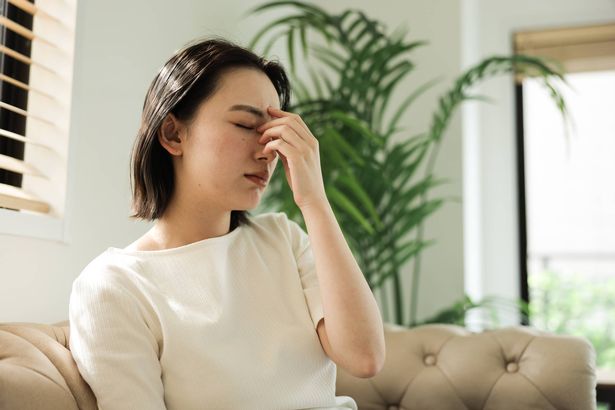 تجلس امرأة شابة على الأريكة في المنزل وهي تحمل الجزء العلوي من أنفها لأنها تشعر بتوعك
