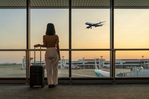 سائح السفر يقف مع أمتعة مشاهدة غروب الشمس في نافذة المطار