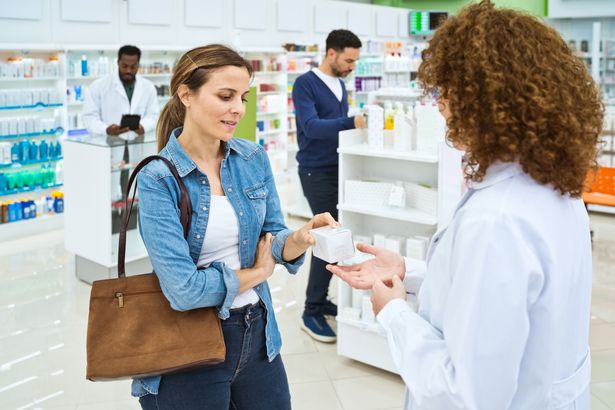 العميل الإناث يتحدث مع الصيدلي ، عقد صندوق الطب في متناول اليد. إنهم يقفون في الصيدلة.