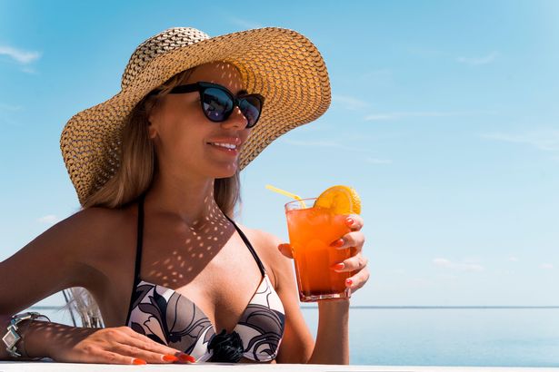 هذه صورة لامرأة شابة ترتدي نظارة شمسية وشمس تحمل كوكتيل