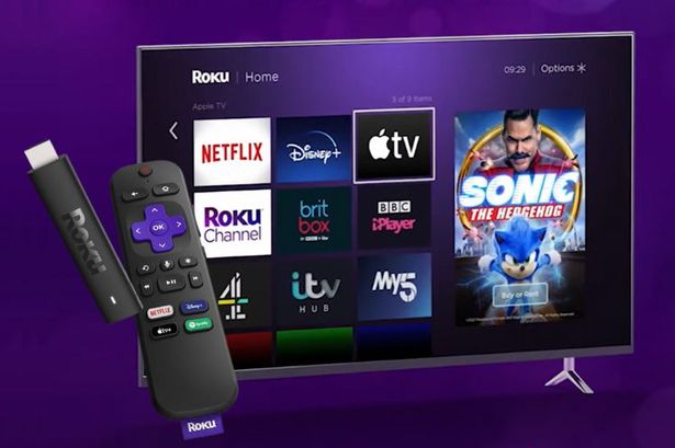 عصا دفق Roku بجوار تلفزيون يعرض شاشة Roku الرئيسية