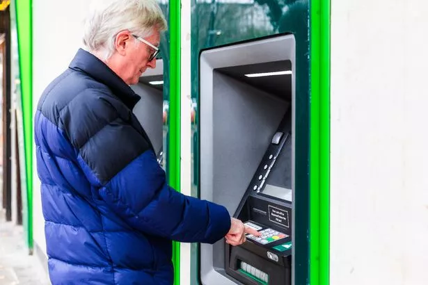 صورة ملونة تصور رجلًا كبيرًا يستخدم آلة ATM في شارع المدينة.