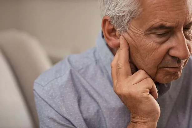 منظر جانبي لرجل كبير مع أعراض فقدان السمع. رجل ناضج يجلس على الأريكة بأصابع بالقرب من آلام الأذن.