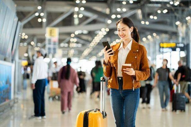 صورة لسيدة الأعمال الشابة الواثقة التي تبتسم في رحلة تجارية جاهزة للهواتف مع الكاميرا مع احتجاز جواز سفر مع تمريرات الصعود إلى التذاكر والهاتف الذكي