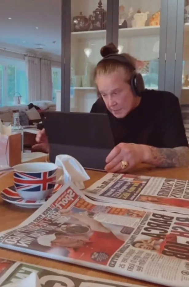 جلس Ozzy Osbourne ، في قمة أسود ، على طاولة مع جهاز لوحي أمامه.