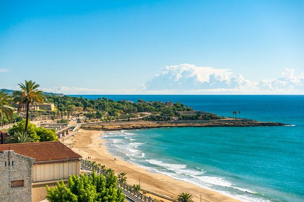 Tarragona ، إسبانيا - 11 أكتوبر ، 2020: منظر لـ Platja del Miracle (Miracle Beach) والبحر الأبيض المتوسط ، مع أنقاض رينا وسانت جوردي على الخلفية ، على سماء زرقاء صافية مشمسة.
