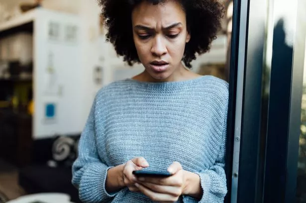 شابة أمريكية من أصل أفريقي تقرأ بعض الأخبار السيئة في المنزل على تطبيق الهاتف الذكي الخاص بها ، مع إلقاء نظرة قلقة على وجهها