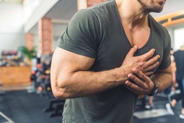 طلقة مقطوعة الرأس على صالة رياضية لرجل قوقازي في منتصف العمر في تي شيرت غير رسمي يمسك يديه على صدره