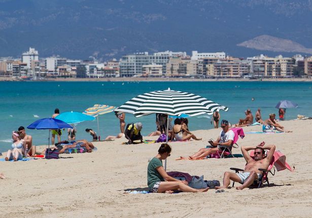 Playa de Palma Beach مع الأشخاص الذين يمسكون بالشمس على الرمال وأفق المدينة في الخلفية.